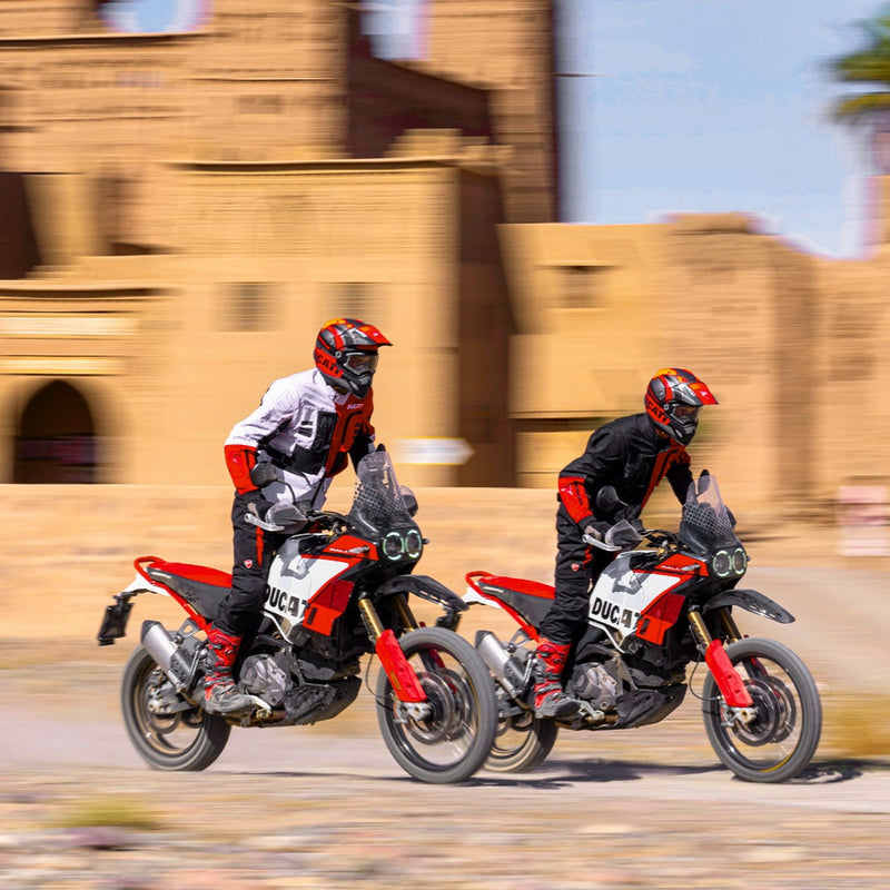 Two people riding Ducati Desert x motorcycles in front of a desert castle.
