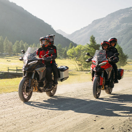 Two Multistrada motorcyclists on a dirt road with mountains in the background