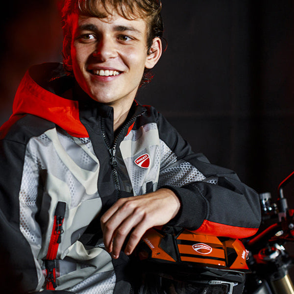 Person wearing a red and gray jacket with a motorcycle in the background