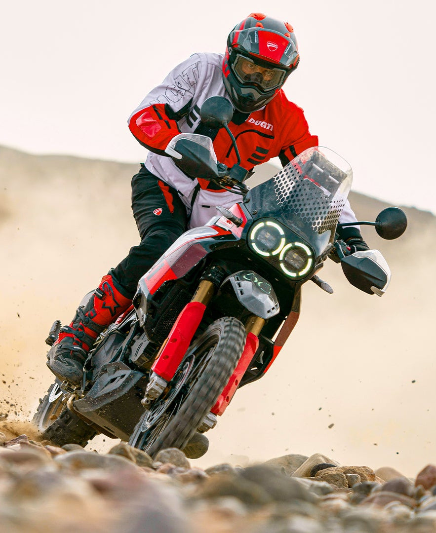 Person riding a red Ducati Desert X motorcycle on a desert trail