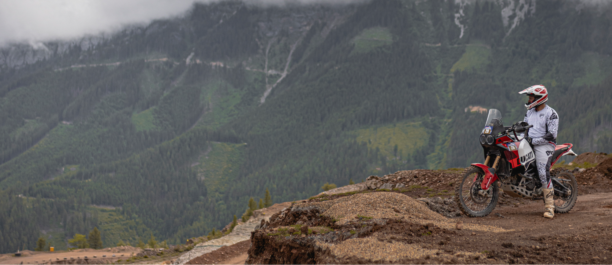 Person on a desertx dirt bike overlooking a mountainous landscape with clouds.